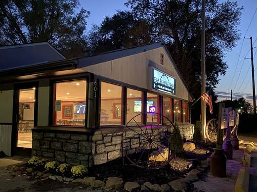 Barbwire Barbecue at dusk, with warm light in the windows, a stone front and an old wagon wheel by the door