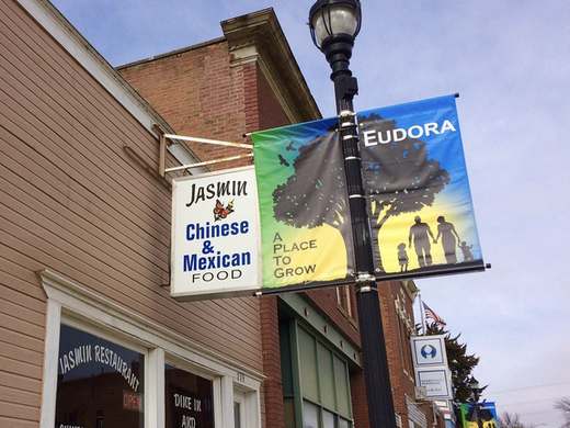 Jasmin Chinese and Mexican Food sign hanging over the sidewalk on Main Street, next to a light pole with an Eudora banner that says A Place to Grow